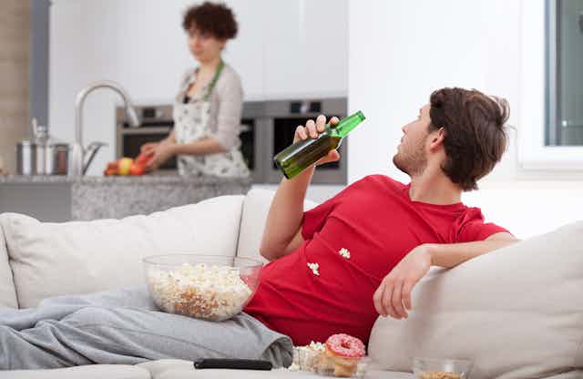 Man on couch with beer, woman in kitchen