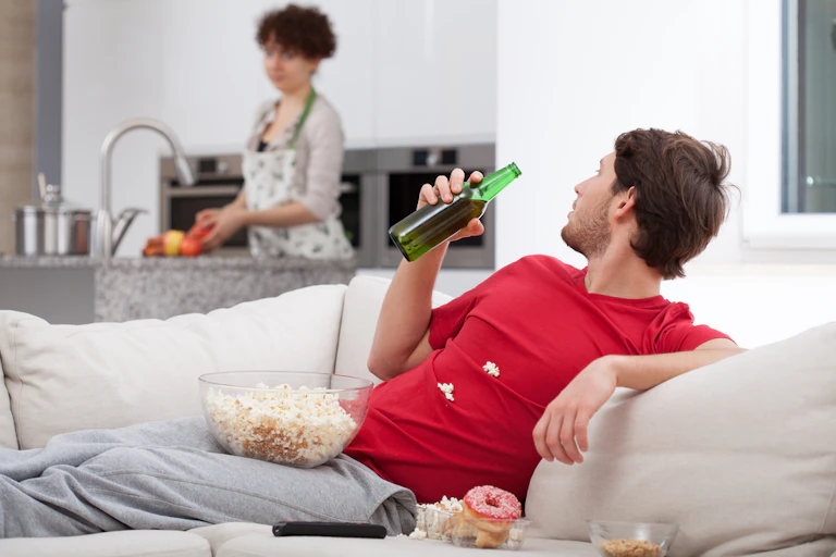 Man on couch with beer, woman in kitchen