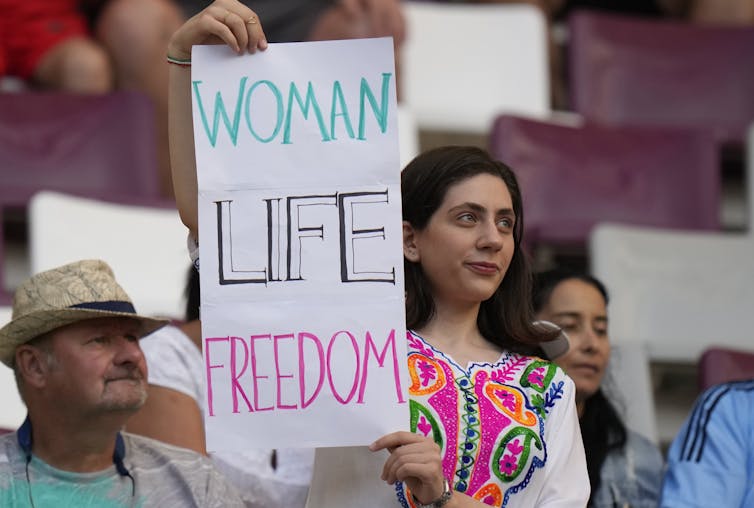 A woman holds up a sign reading Woman Life Freedom.