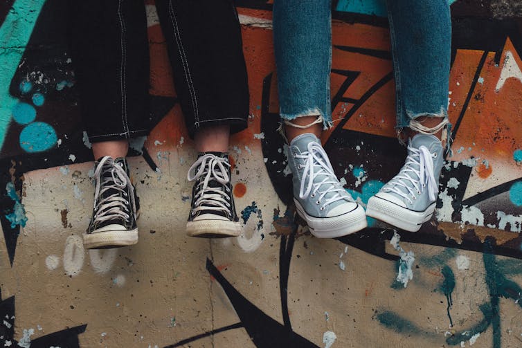 two pairs to feet in sneakers against graffitied wall