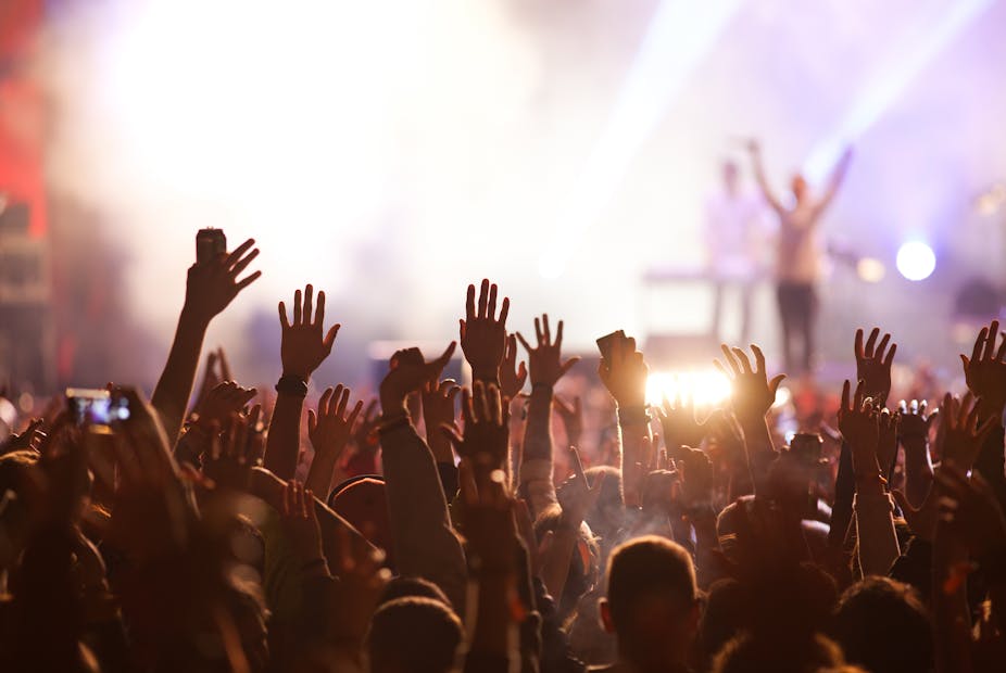 A group of people raise their hands in the air at a concert.