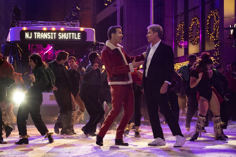 A bright bus lights dancers in the foreground, including Ryan Reynolds in a Santa outfit, and Will Ferrell in a black suit.