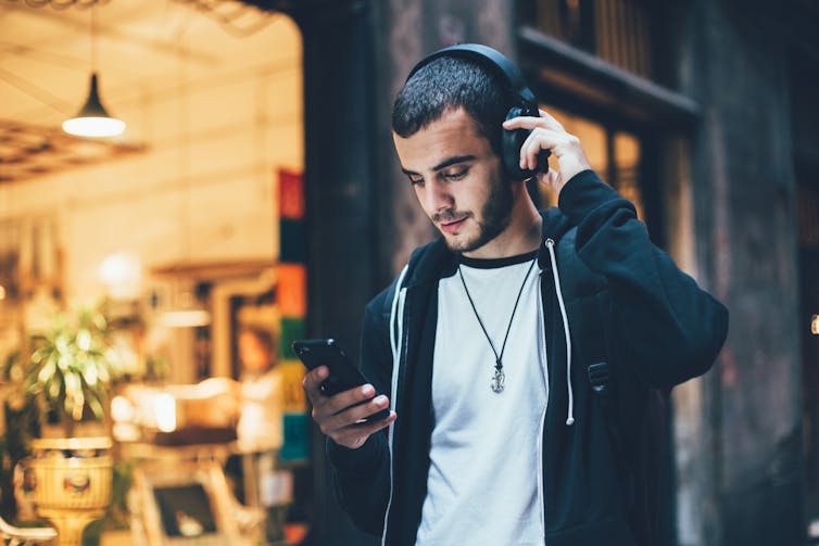 A young man looks at his phone while wearing headphones.