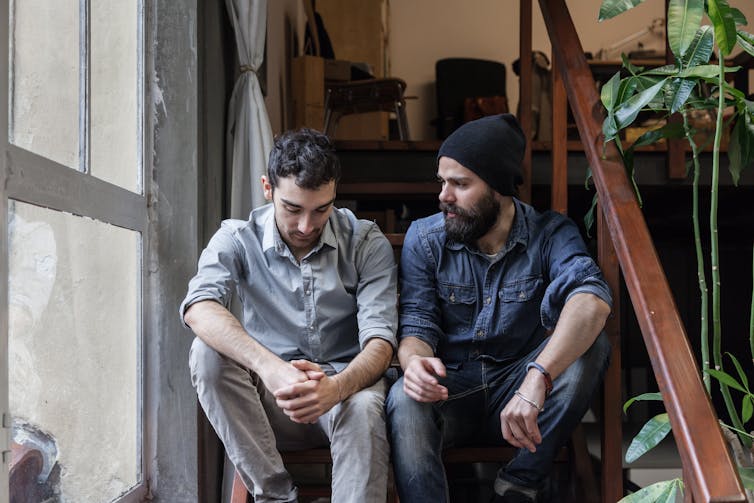 Two young men sitting on stairs talking.