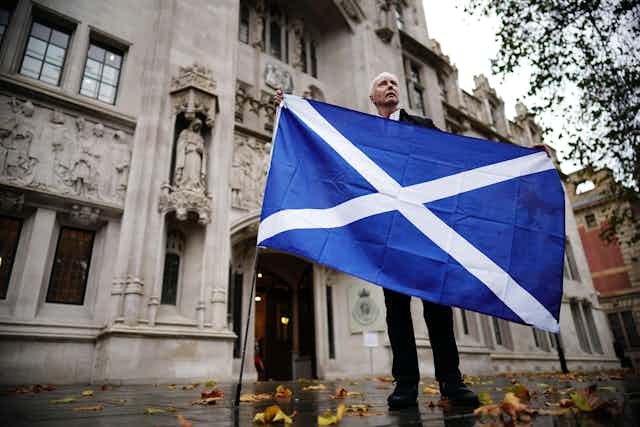 A man holding a Scottish flag standing in front of the Supreme Court in London. 