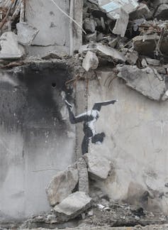 A stencil Banksy work depicting a gymnast doing a handstand on the side of a bombed building in Ukraine.