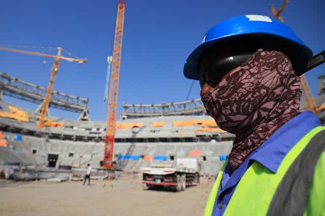 A construction worker covers  his face with a scarf, sunglasses and hard-hat.