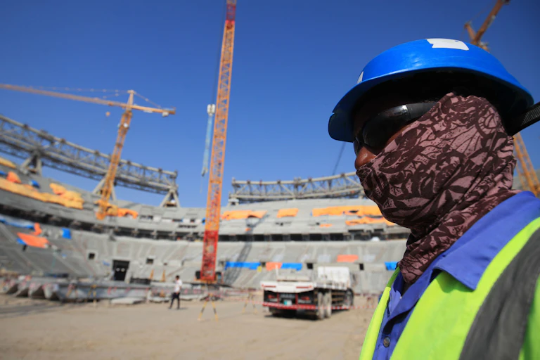 A construction worker covers his face with a scarf, sunglasses and hard-hat.