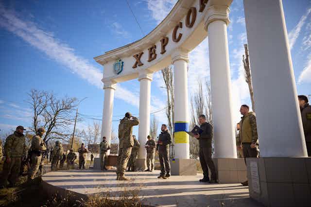 A Ukrainian soldier salutes Ukrainian president Volodymyr Zelensky at the gates of IKherson after its recapture, November 2022.