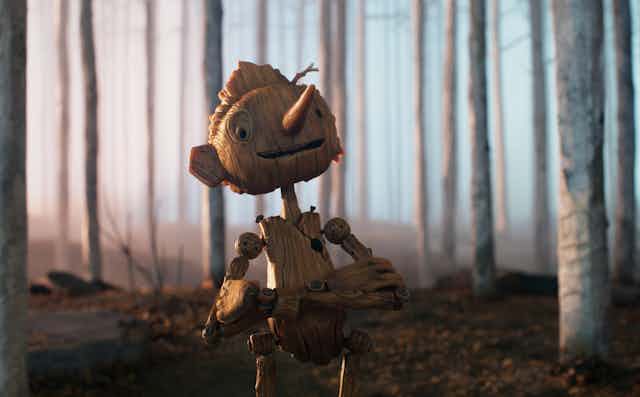 Pinocchio, made from rough wood, stands in woodland