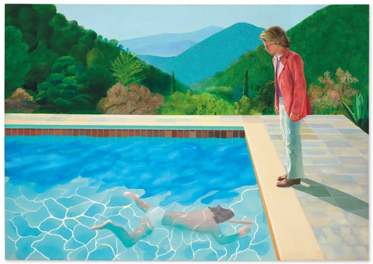 Swimming pool with swimmer and hills in background with a man standing watch.