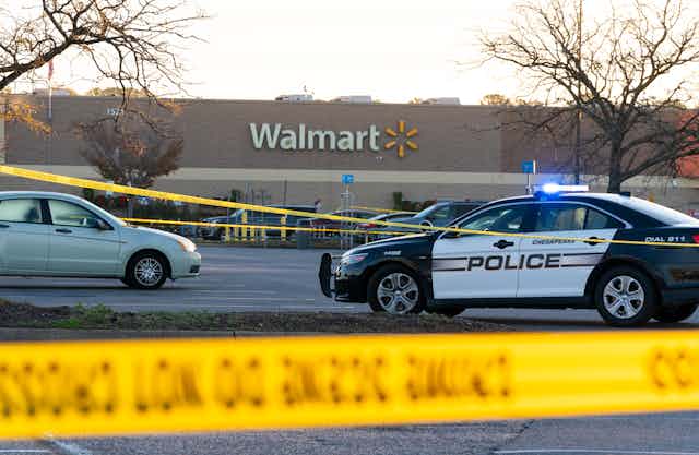 Yellow police tape hang in the foreground in front of police cars and a store with 'Walmart' on the facade.