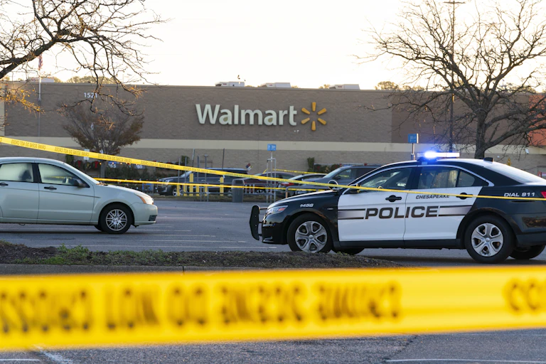 Yellow police tape hang in the foreground in front of police cars and a store with 'Walmart' on the facade.