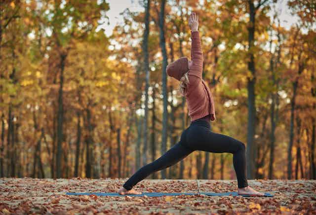 Photo d’une  femme pratiquant le yoga dans un bois, par une belle journée d’automne.