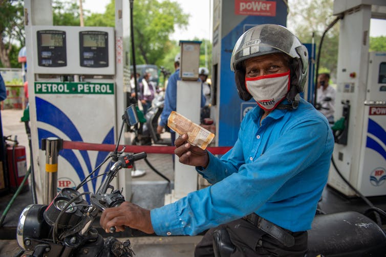 A motorcylist brandishes a rupee note in front a petrol pump.
