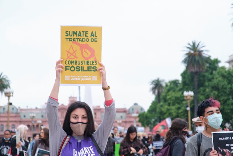 A woman holds a sign saying 'join the fossil fuel treaty' in Spanish.