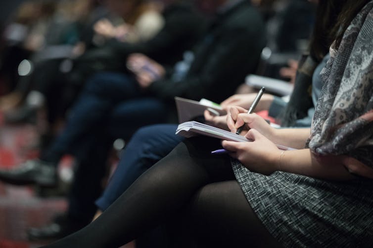 a row of people seated and holding notebooks and pens