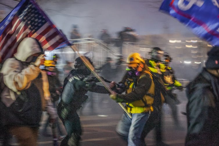 Policía y alguien que sostiene una bandera estadounidense, peleando.