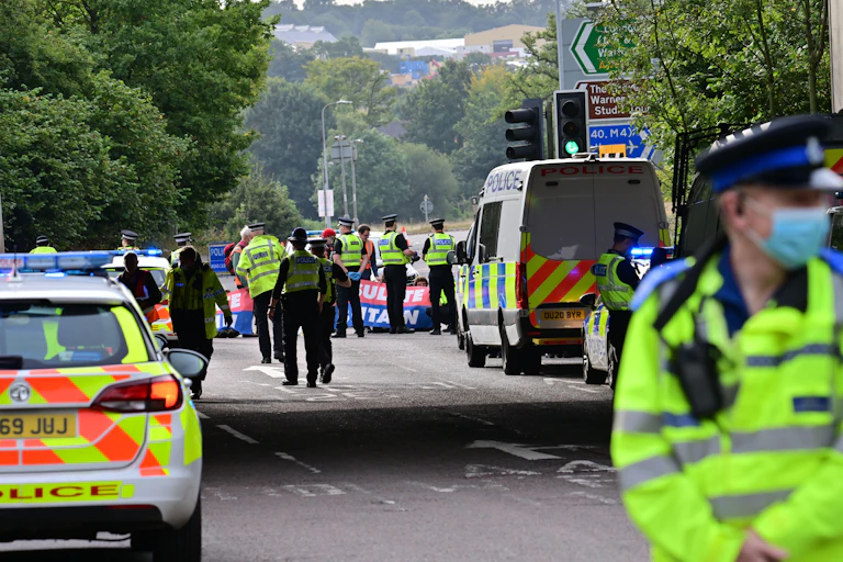 A police car parked and officers in uniform with high vis jackets.