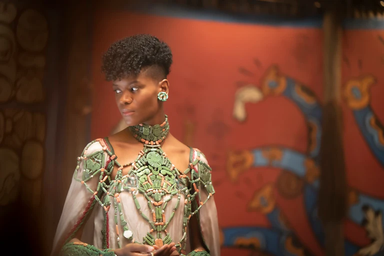 Woman wearing armour stands against a tapestry.
