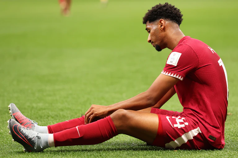 A Qatari player sits on the pitch adjusting his sock.