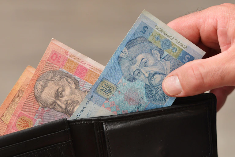 A hand pulls Ukrainian bank notes out of a wallet.