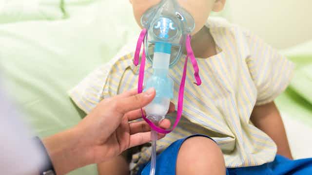 a toddler with an oxygen mask on held to their face
