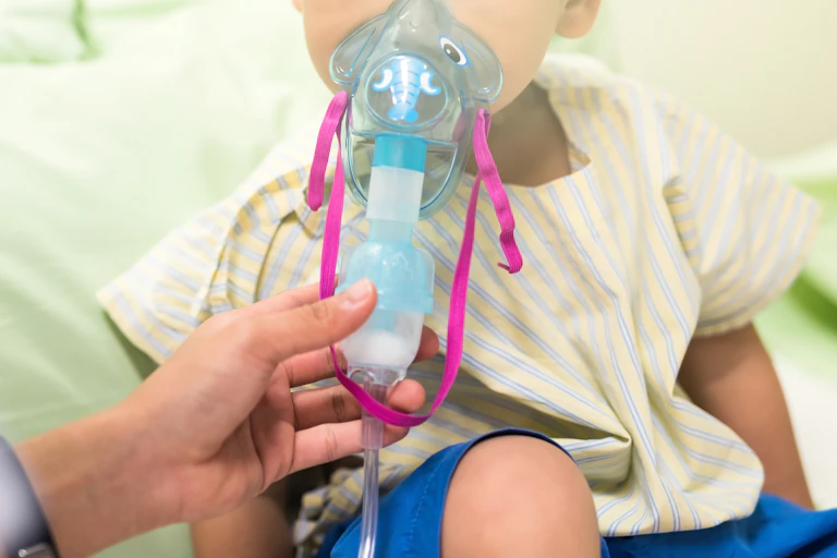 a toddler with an oxygen mask on held to their face