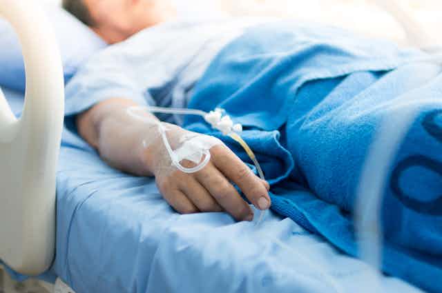 Person lying in hospital bed with tubes in hand