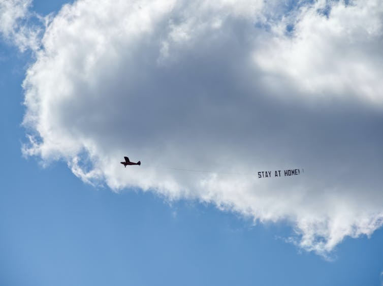 small plane in sky with 'stay home' banner behind it