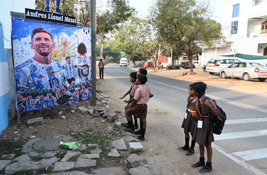 Des écoliers s'arrêtent devant un panneau dressé en honneur du joueur argentin Lionel Messi à Hyderabad, au sud de l'Inde, le 25 novembre 2022.  