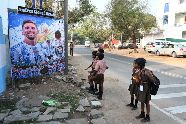 Des écoliers s'arrêtent devant un panneau dressé en honneur du joueur argentin Lionel Messi à Hyderabad, au sud de l'Inde, le 25 novembre 2022.