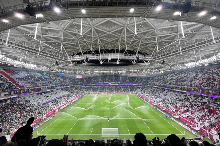 A football stadium with lights and sprinklers on the grass.