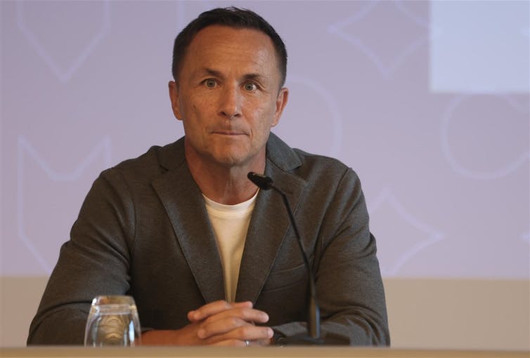 Dennis Wise sits in front of a small microphone wearing a suit.