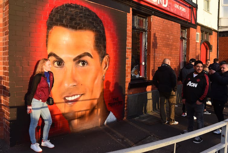 Fans pose and walk past a mural of Cristiano Ronaldo's face on the wall of a pub outside the Old Trafford stadium