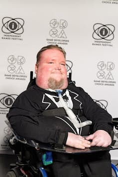 Steven Spohn in a tuxedo in a wheelchair on the Game Developers Conference red carpet