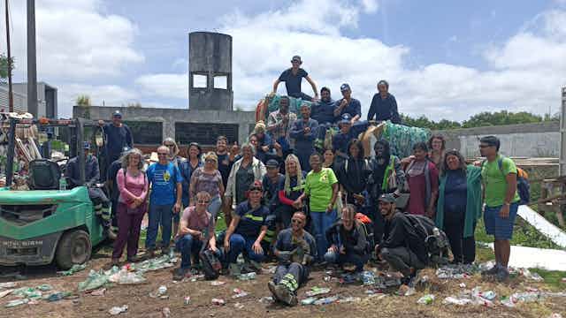 A group of people posing in front of a building with plastic waste strewn on the ground.