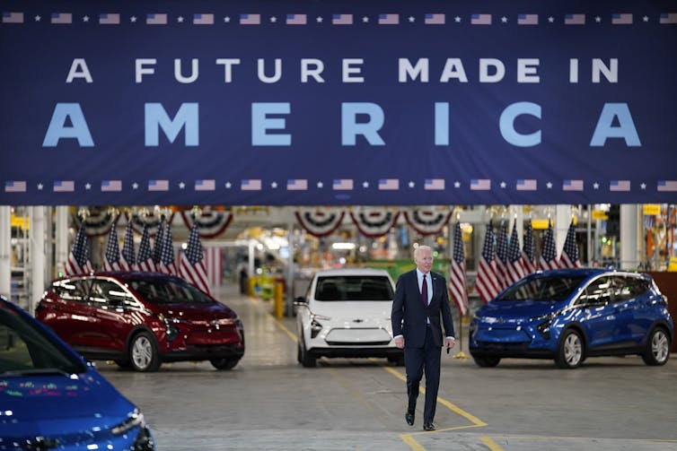 man insult walks in front of cars under sign reading 'A future made in America'