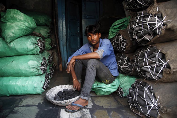 man sits in front of bags of coal
