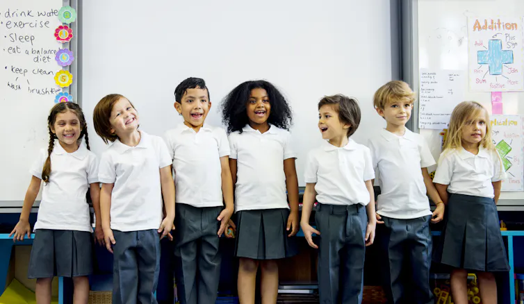 Young students line up against a whiteboard.