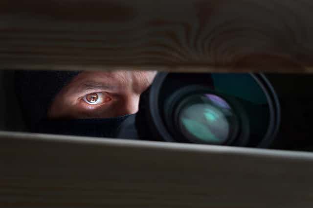 Man's eye and camera lens seen through a narrow slit