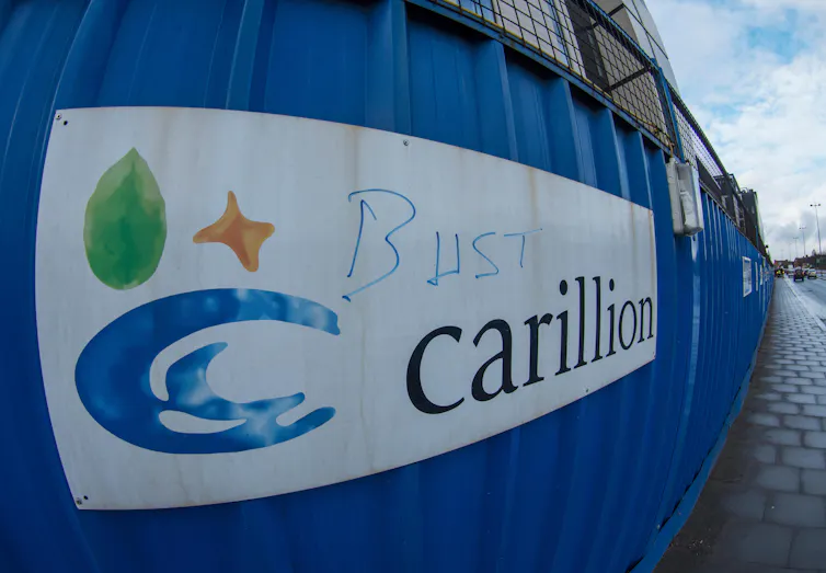 A wall with a Carillion logo with 'bust' in graffiti over the top