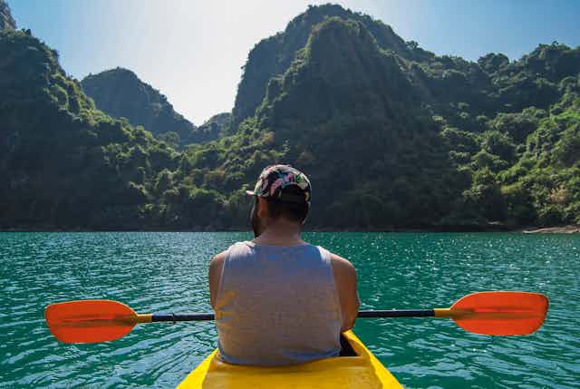 A man paddling a yellow kayak in bright blue sea surrounded by picturesque mountains