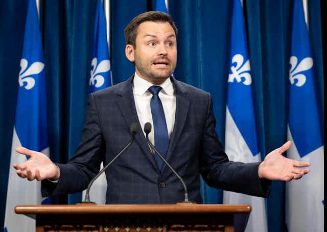 Paul St-Pierre-Plamondon parle devant des micros, avec des drapeaux du Québec en arrière-plan