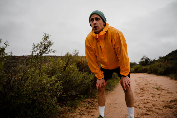 Un homme, en protection de pluie et bonnet, s’est arrêté en plein running, visiblement épuisé