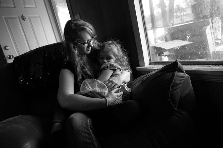 Black and white photo of a young woman smiling down at a girl, who she is holding in her arms on a couch