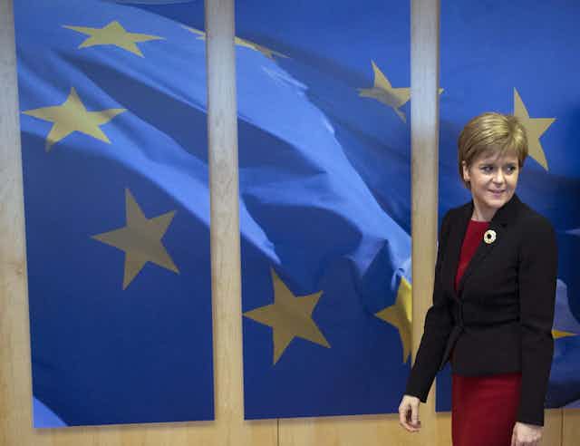 Nicola Sturgeon walking in front of a picture of the European flag. 