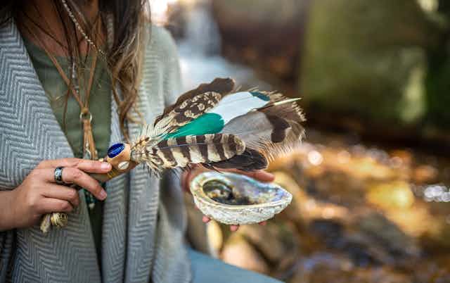 A woman holding feathers and a bowl performing a smudging ceremony.