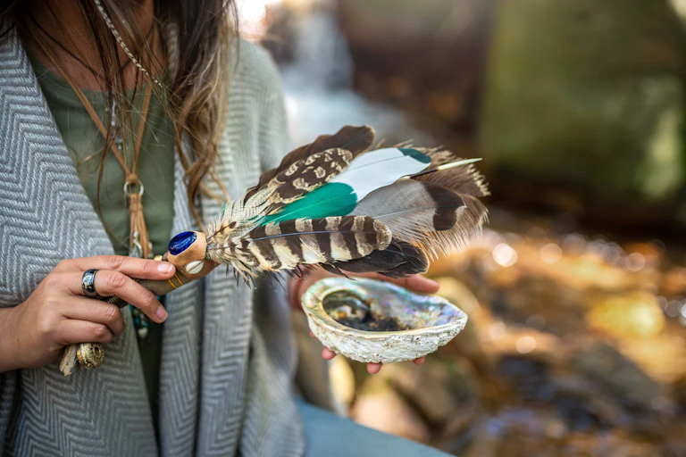 A woman holding feathers and a bowl performing a smudging ceremony.