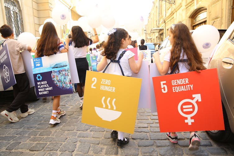 Unas niñas de espaldas llevan carteles con los Objetivos de Desarrollo Sostenible.